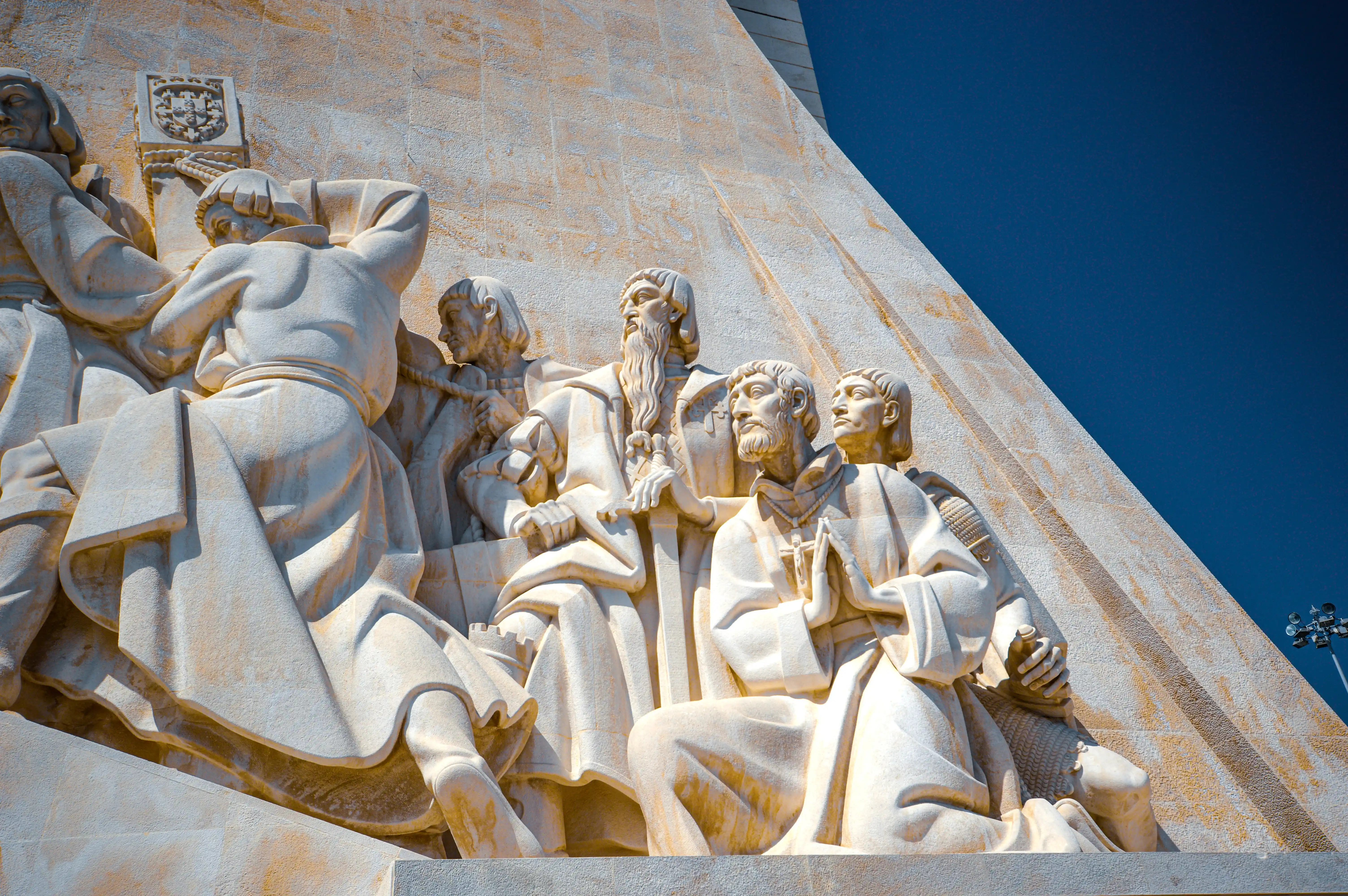 Close-up view of detailed stone sculptures of men in historical dress on a monument, set against a bright blue sky.